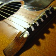 closeup photo of acoustic guitar bridge, sound hole with strings and pegs