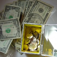 photo of a variety of dollar bills with a glass box full of coins