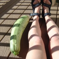 Photo of a woman's legs with a giant zucchini in sunshine