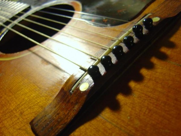 closeup photo of acoustic guitar bridge, sound hole with strings and pegs