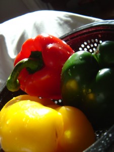 three bell peppers in a collander in the sunlight