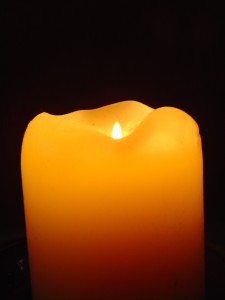 photo of orange candle with flame burning in the darkness