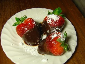 plate with three chocolate covered strawberries with powdered sugar