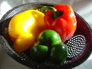 photo of a kitchen collander with three red yellow and green bell peppers