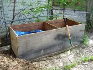 photo of a two compartment compost bin with a pitchfork leaning up against it