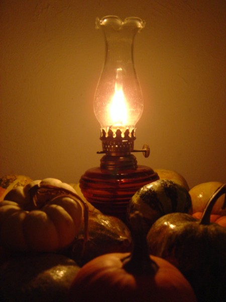 photo of burning oil lamp surrounded by various fall squash and gourds