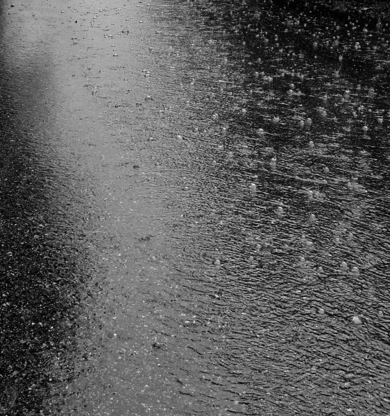 photo of raindrops falling on wet pavement with ripples and bubbles