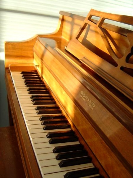 photo of a golden brown spinet upright piano with a sunbeam