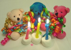 Photo of three teddy bears with colorful birthday ribbons and candles