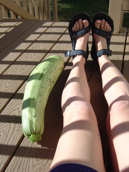 Photo of a woman's legs with a giant zucchini in sunshine