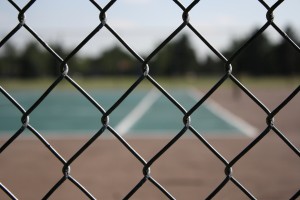 close up photo of chain link fence with tennis court in the background