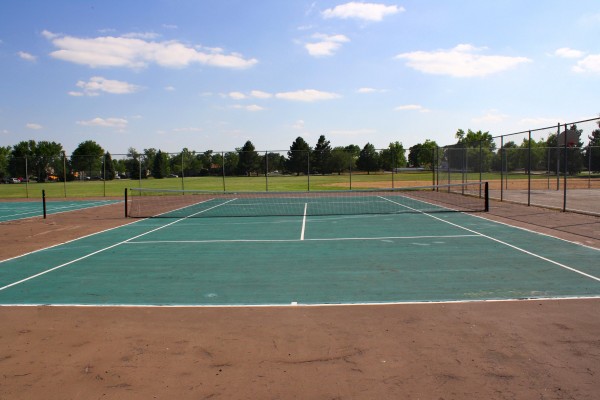 Free photo of a tennis court with grass, trees and blue sky in the background